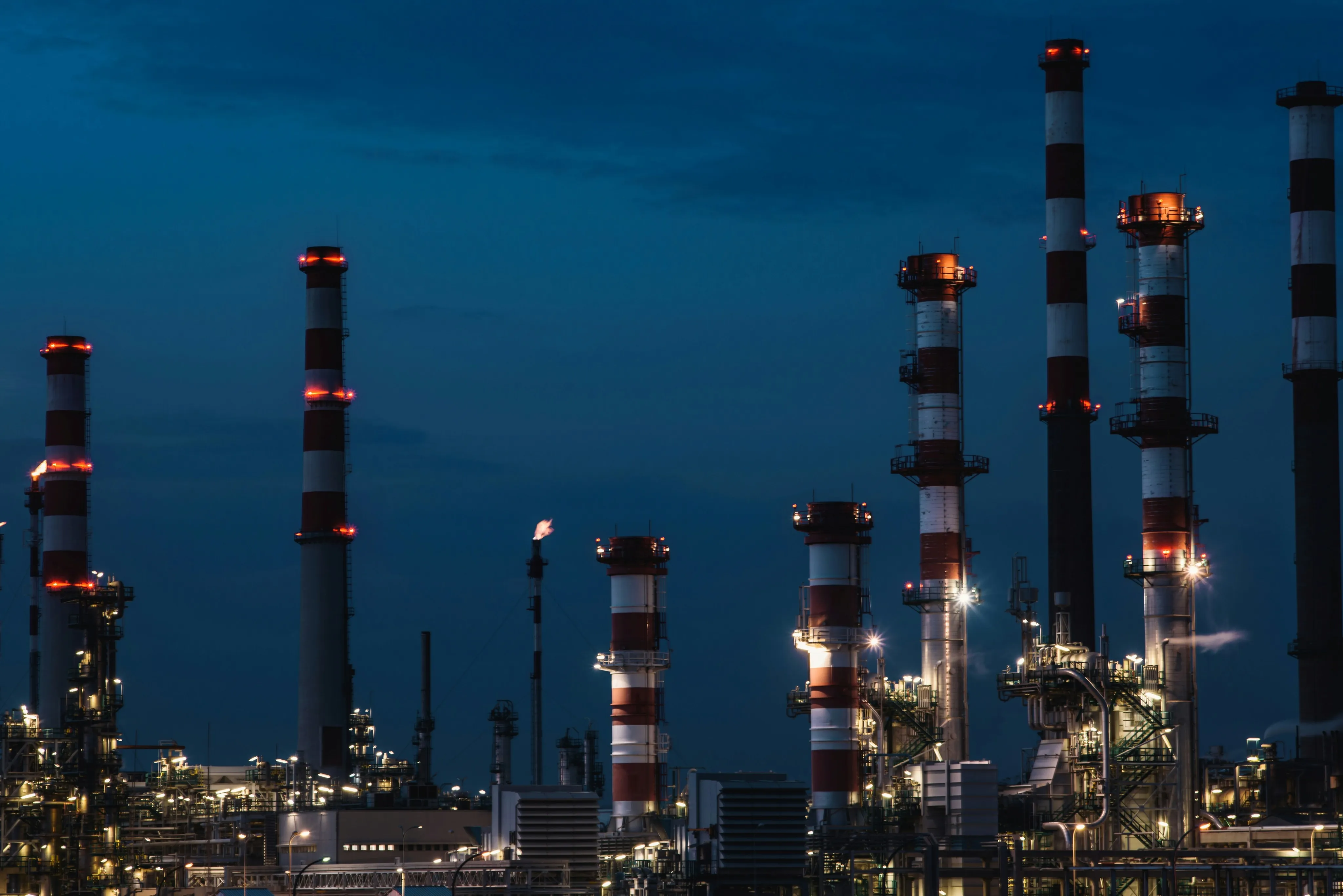 Oil and gas refinery towers lit at dusk.